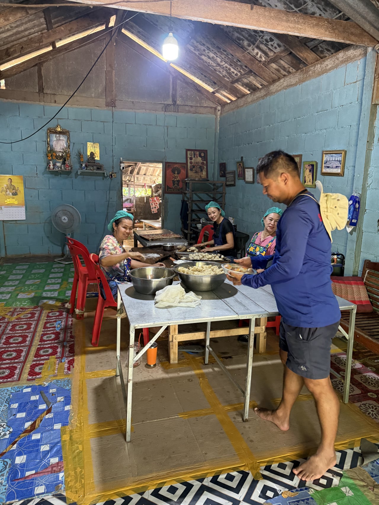 Thajské ženy v síťkách připravují jídlo u stolu, muž nese misku.