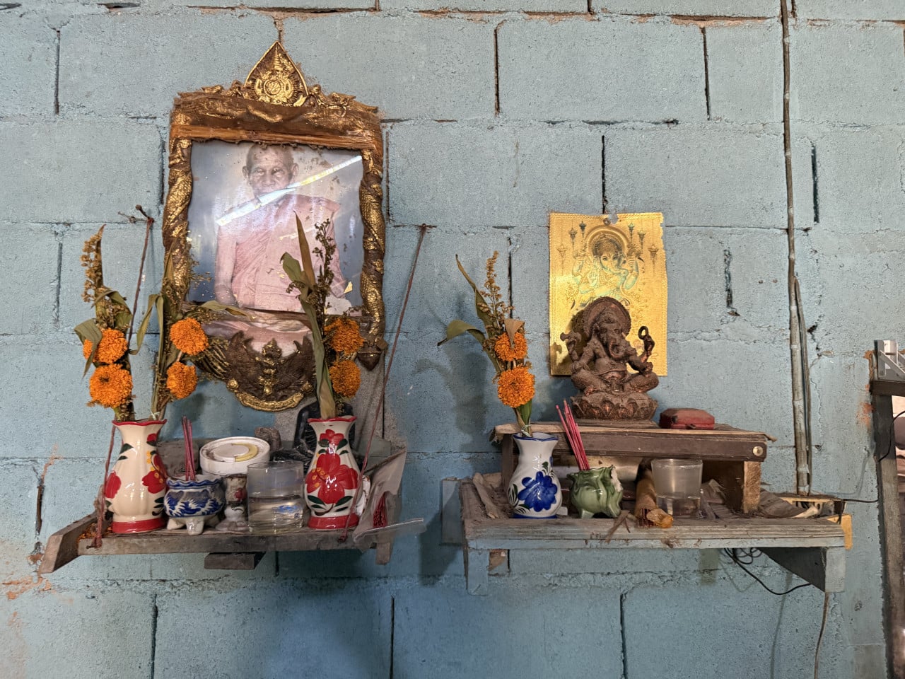 Domácí oltář na modré zdi: portrét mnicha, Ganéša, květiny a vonné tyčinky