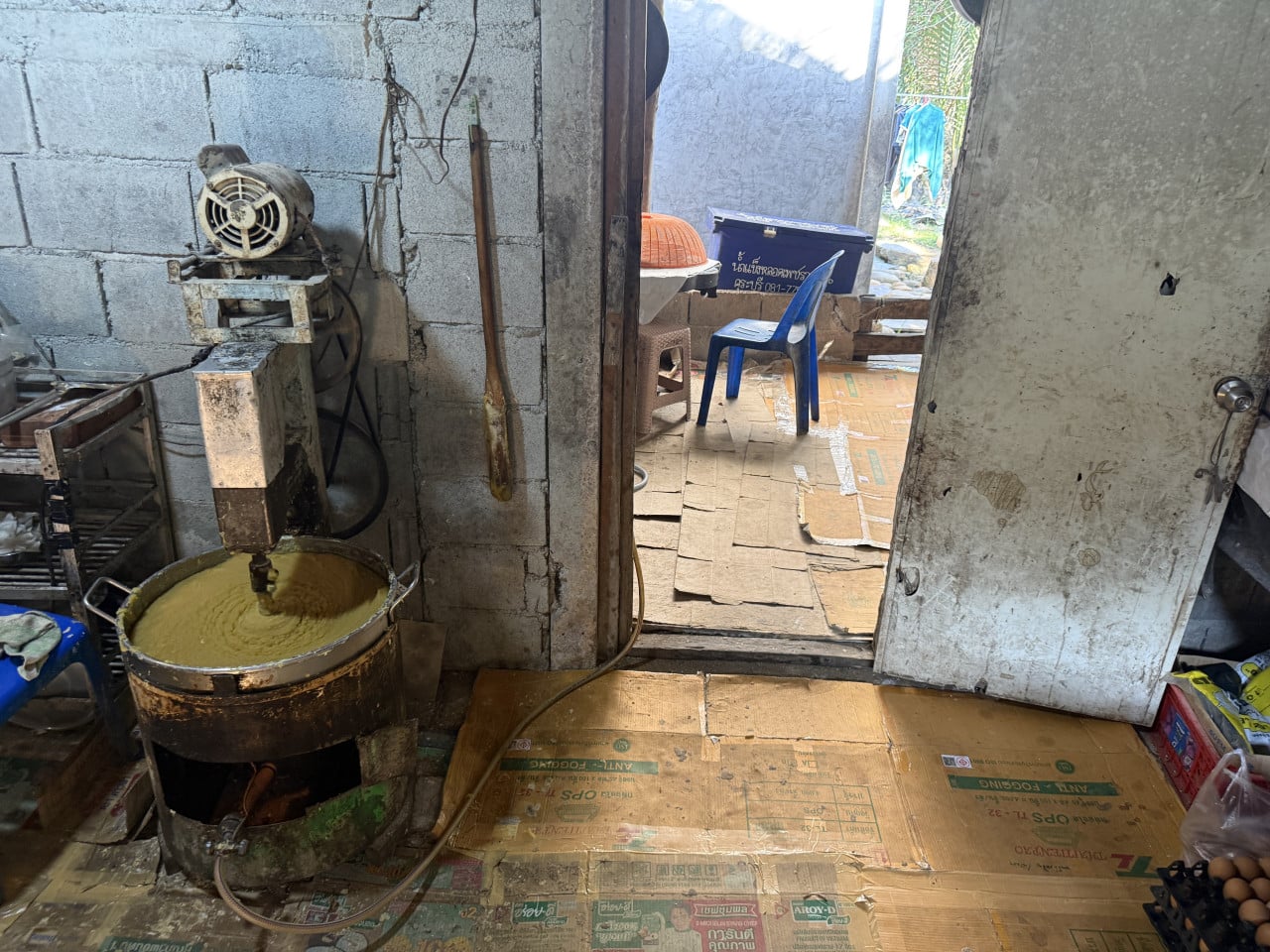 Míchadlo v kovovém kotli míchá těsto, kartony, modrá židle, thajský nápis.