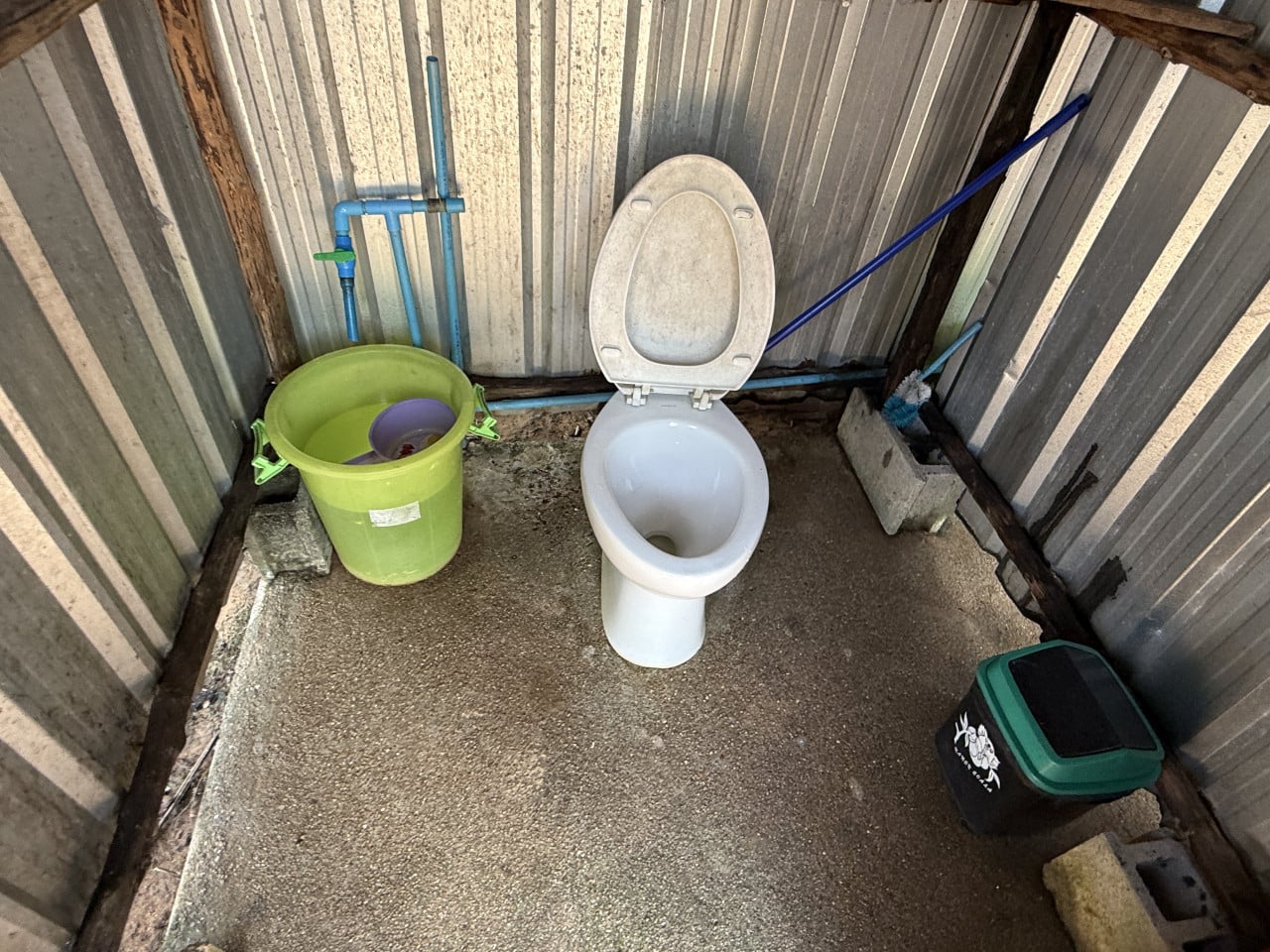 Jednoduchý záchod v plechové kóji, WC mísa, zelený kbelík a mop