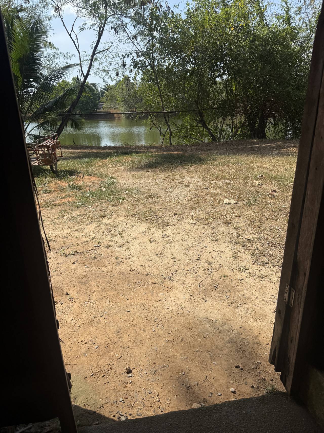 Pohled z přístřešku na prašný dvůr, řeku a stromy v pozadí.