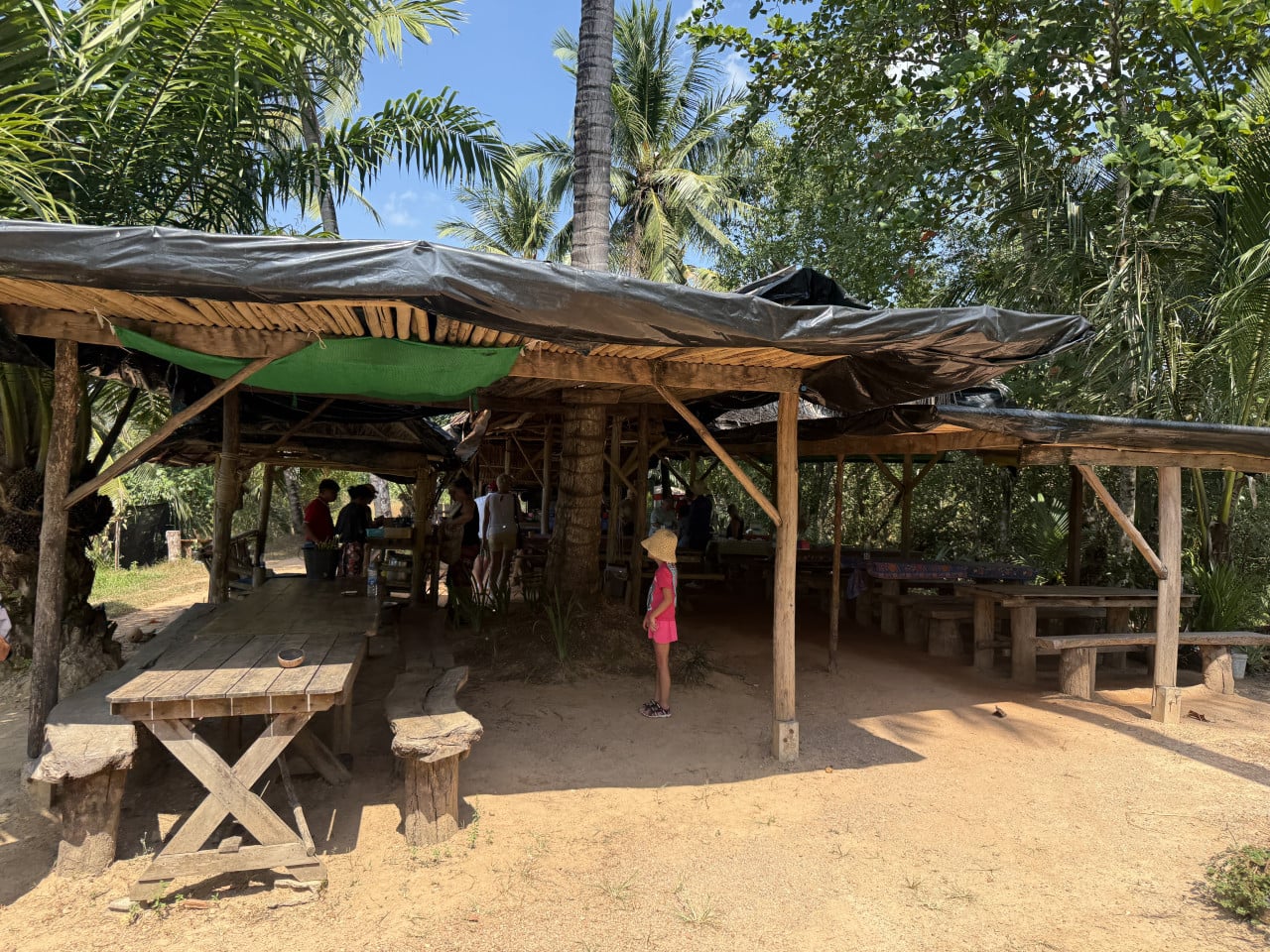 Otevřený dřevěný přístřešek s lavicemi v džungli, uvnitř lidé a dítě