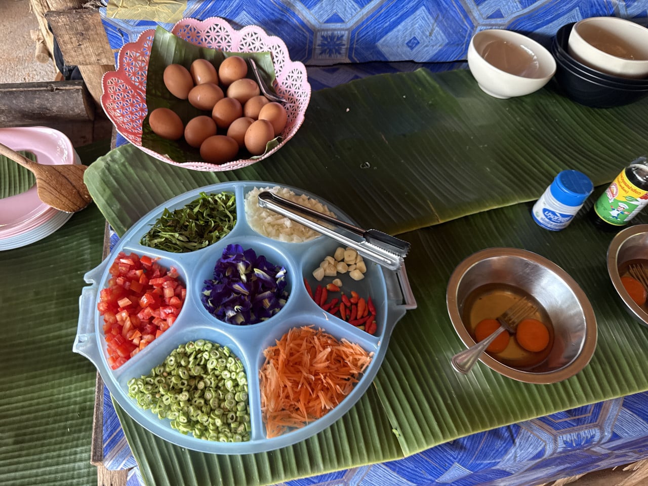 Modrý talíř s nakrájenou zeleninou a fialovými květy, vedle vejce a miska s vejci
