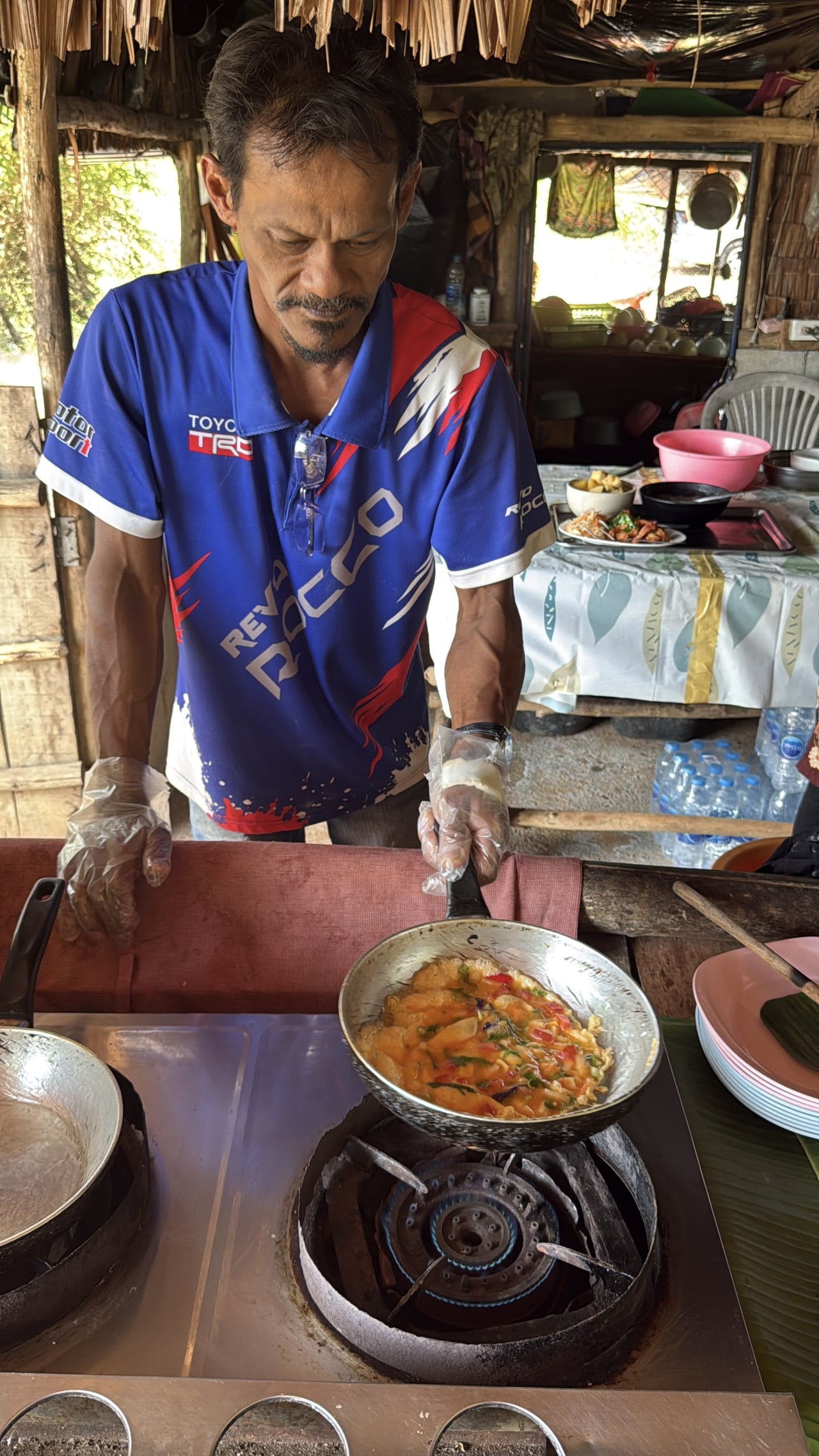 Muž v tričku TOYOTA TRD, REVO ROCCO smaží omeletu na plynovém vařiči.