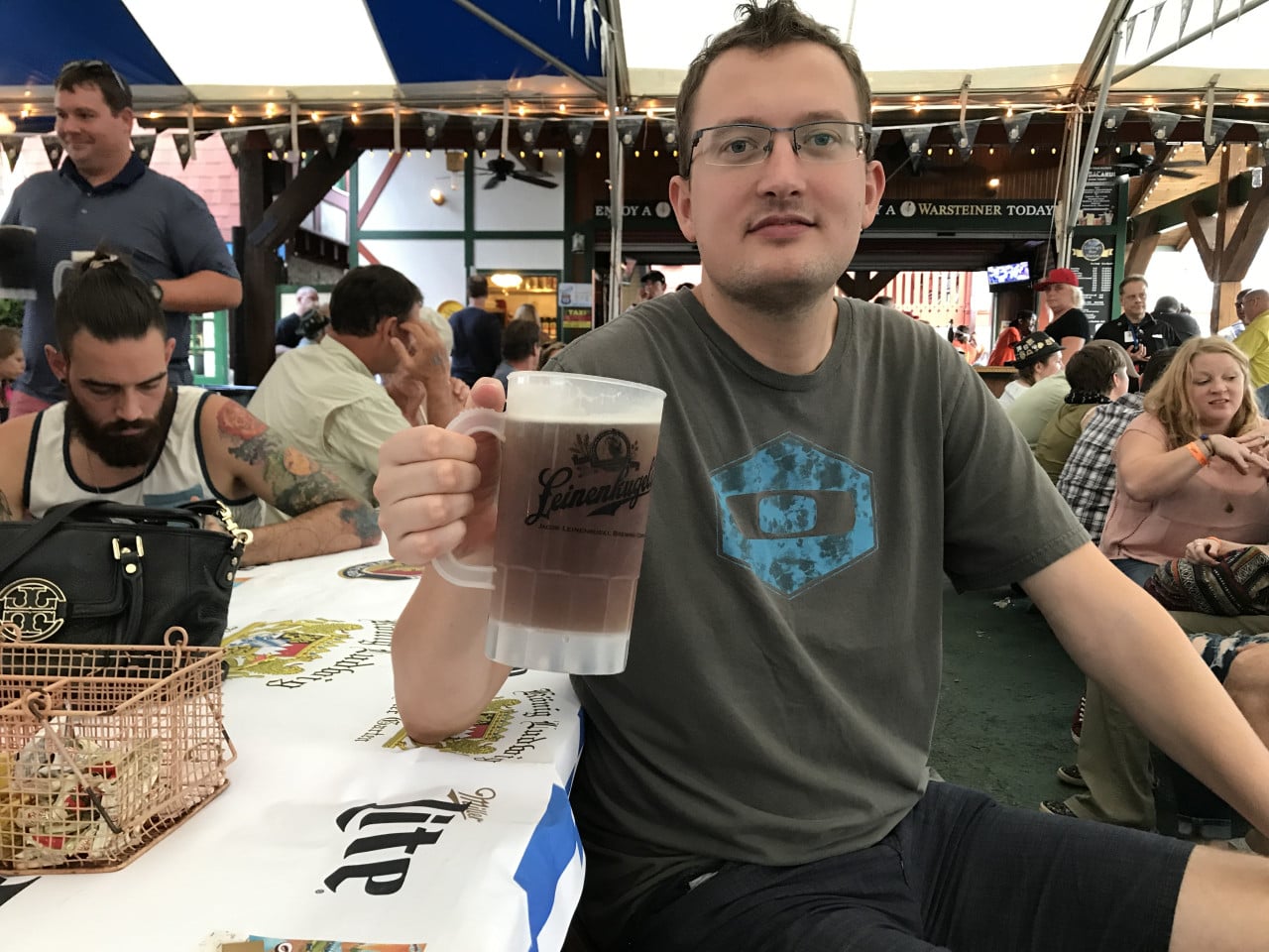 Muž na Oktoberfestu v Helen drží půllitr piva u stolu mezi lidmi.