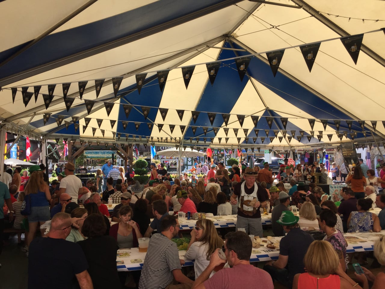 Rušný Oktoberfestový stan s lidmi u stolů, pivem a bavorskou výzdobou