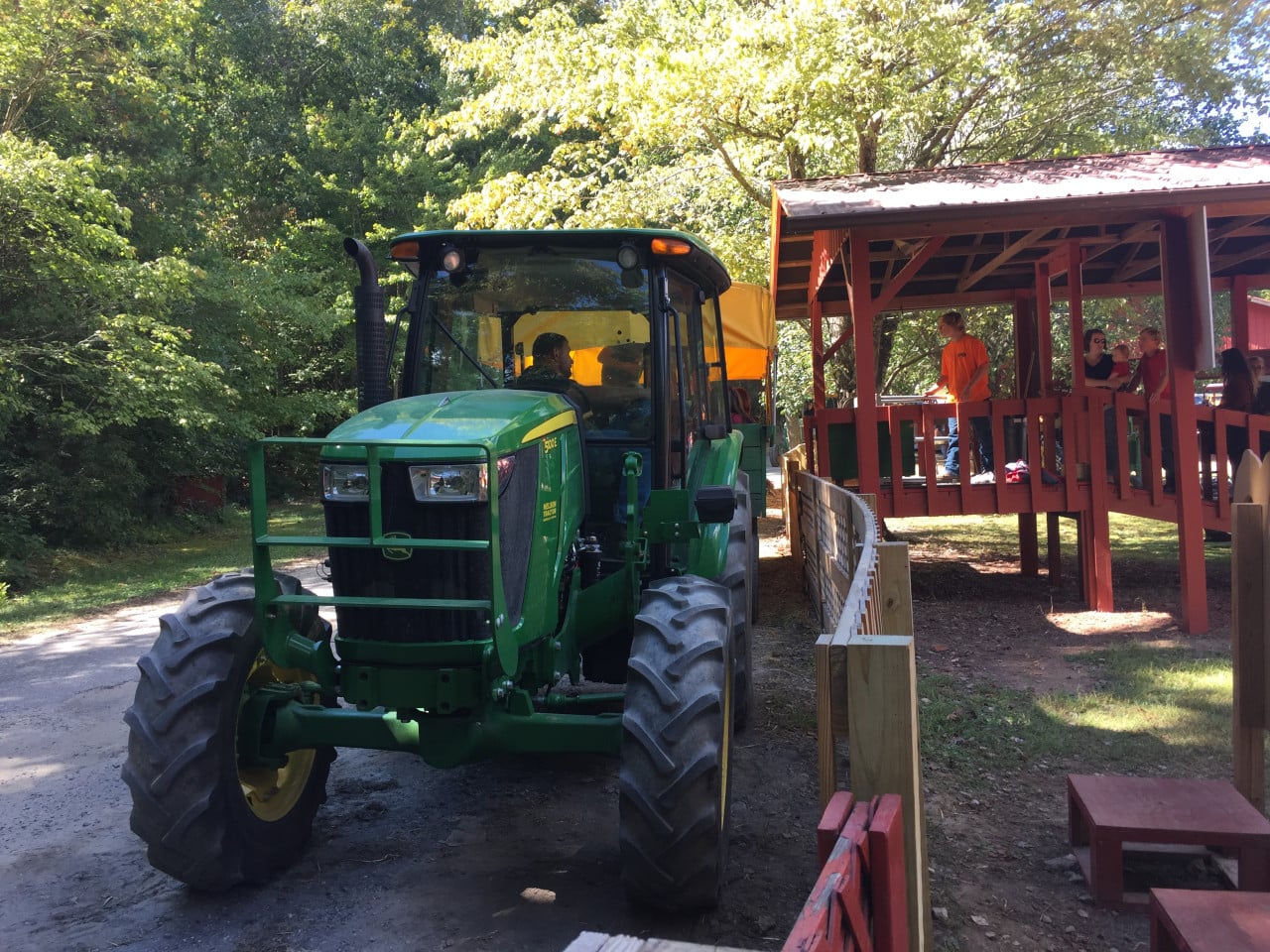 Zelený traktor projíždí kolem dřevěného pavilonu s lidmi na Oktoberfestu.