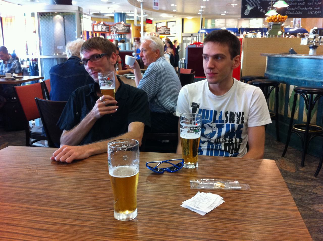 Dva muži u stolu s pivy Heineken; na stole brýle, účtenky.