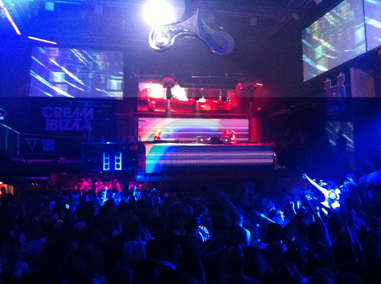 Dav v nočním klubu před DJe na pódiu, světelné projekce a nápis CREAM IBIZA