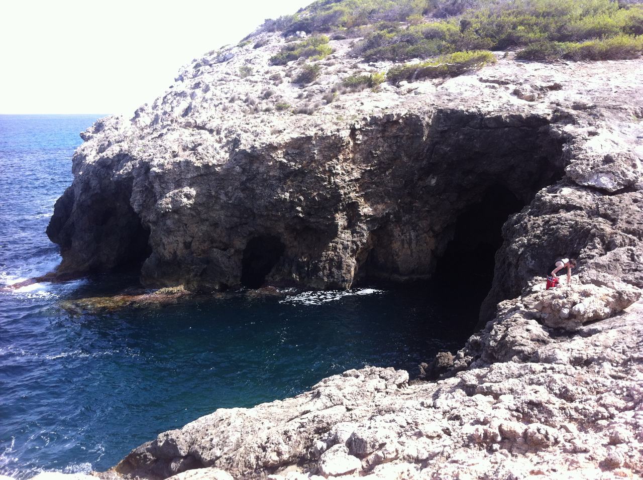 Skalnatý útes s mořskou jeskyní nad modrou vodou, člověk na okraji