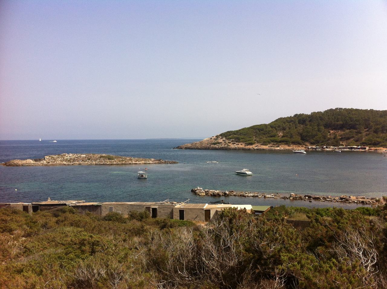 Zátoka s modrým mořem, malé lodě, skalnaté pobřeží a zelený kopec