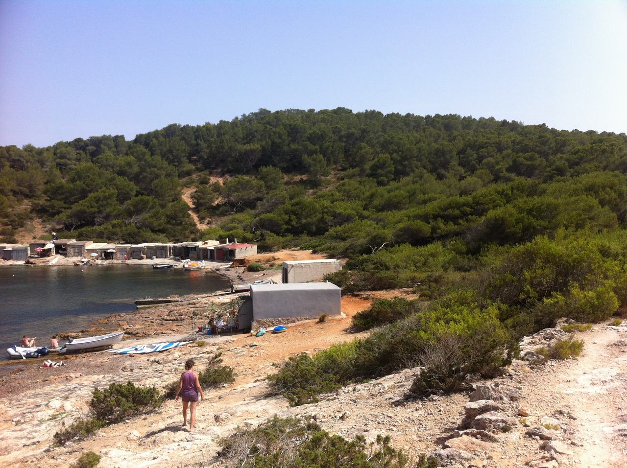 Skalnatá zátoka s malými domky a loďkami, žena schází k vodě