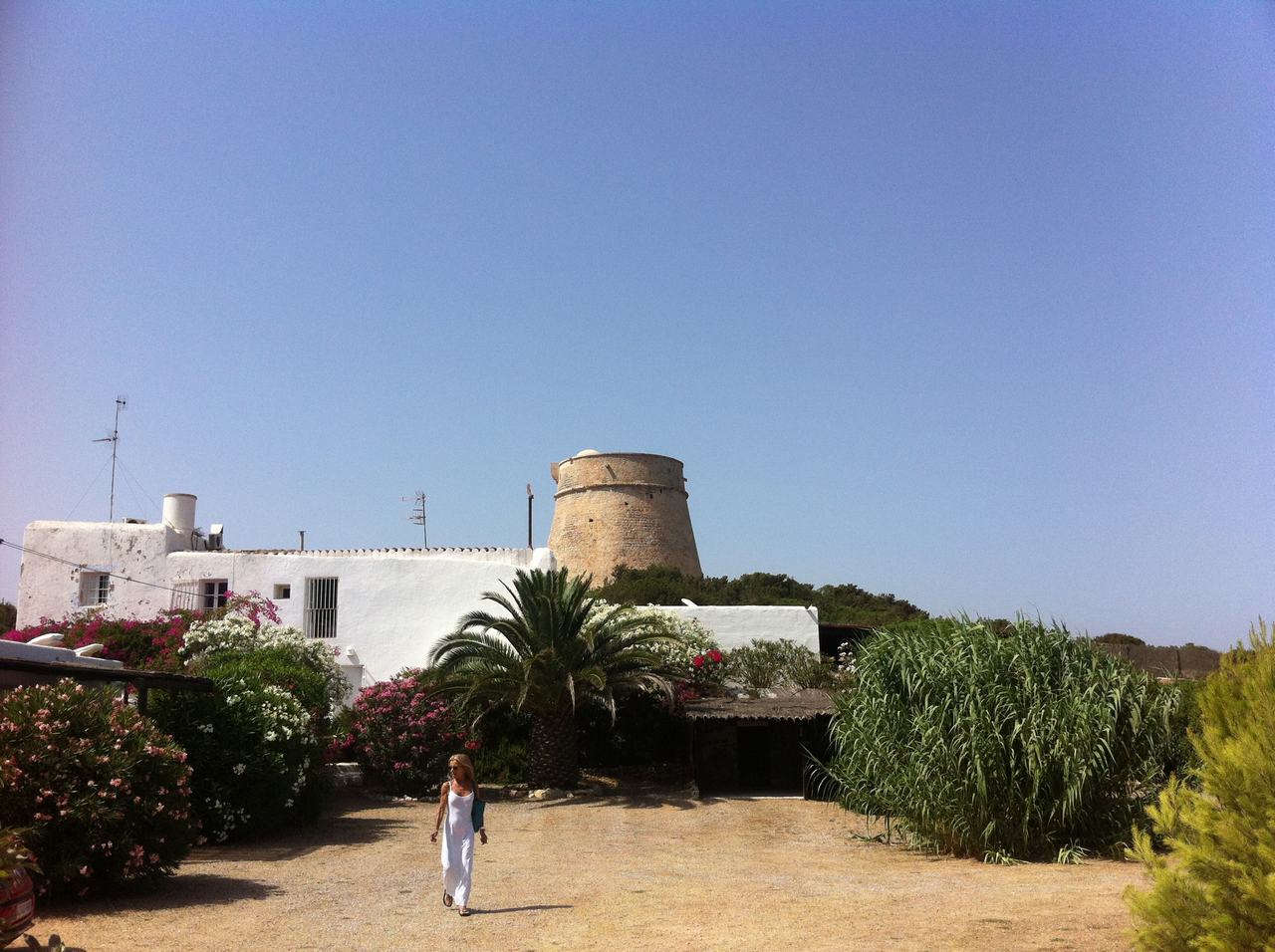 Bílý dům s kamennou věží, palmy a žena kráčí po dvoře