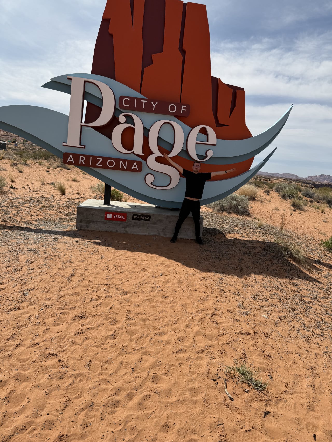 Muž stojí před cedulí CITY OF Page ARIZONA uprostřed pouště