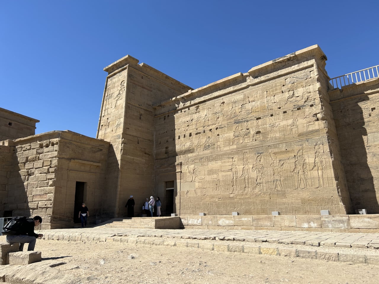 Kamenný chrám Philae s hieroglyfy a návštěvníky pod modrou oblohou
