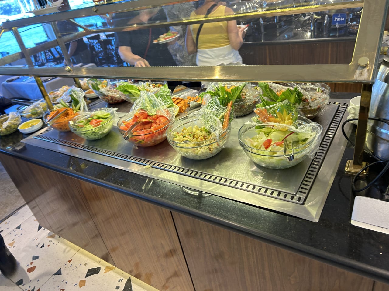 Bufet se saláty v hotelové restauraci, lidé si nabírají jídlo.