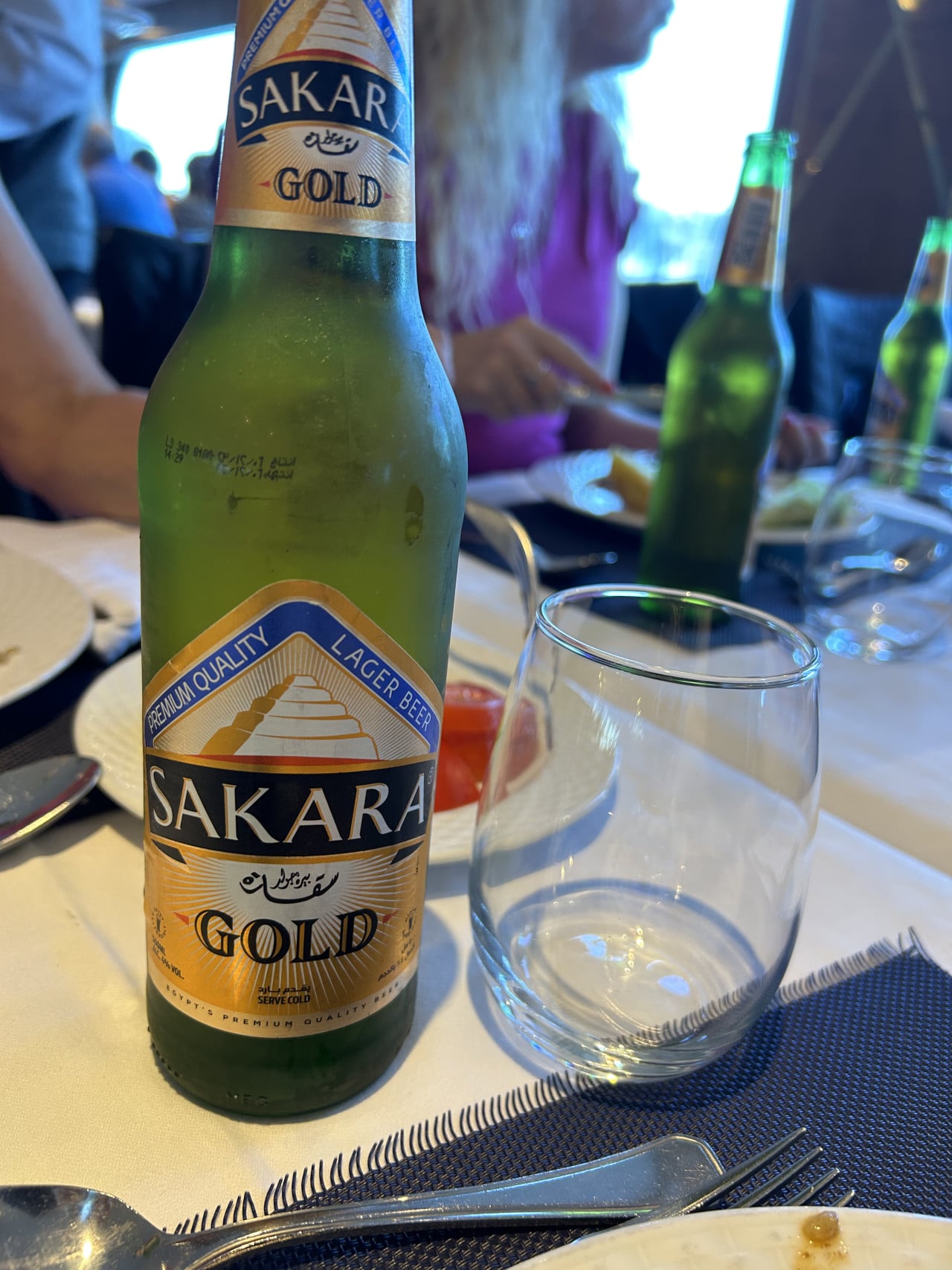 Láhev piva Sakara Gold na stole v restauraci, vedle prázdné sklenice.