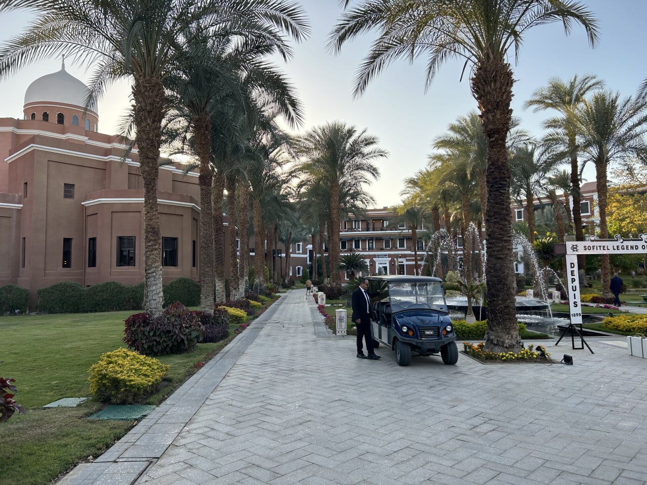Hotelový areál v Asuánu s palmami, cestou, golfovým vozíkem a nápisem Sofitel Legend Old Cataract