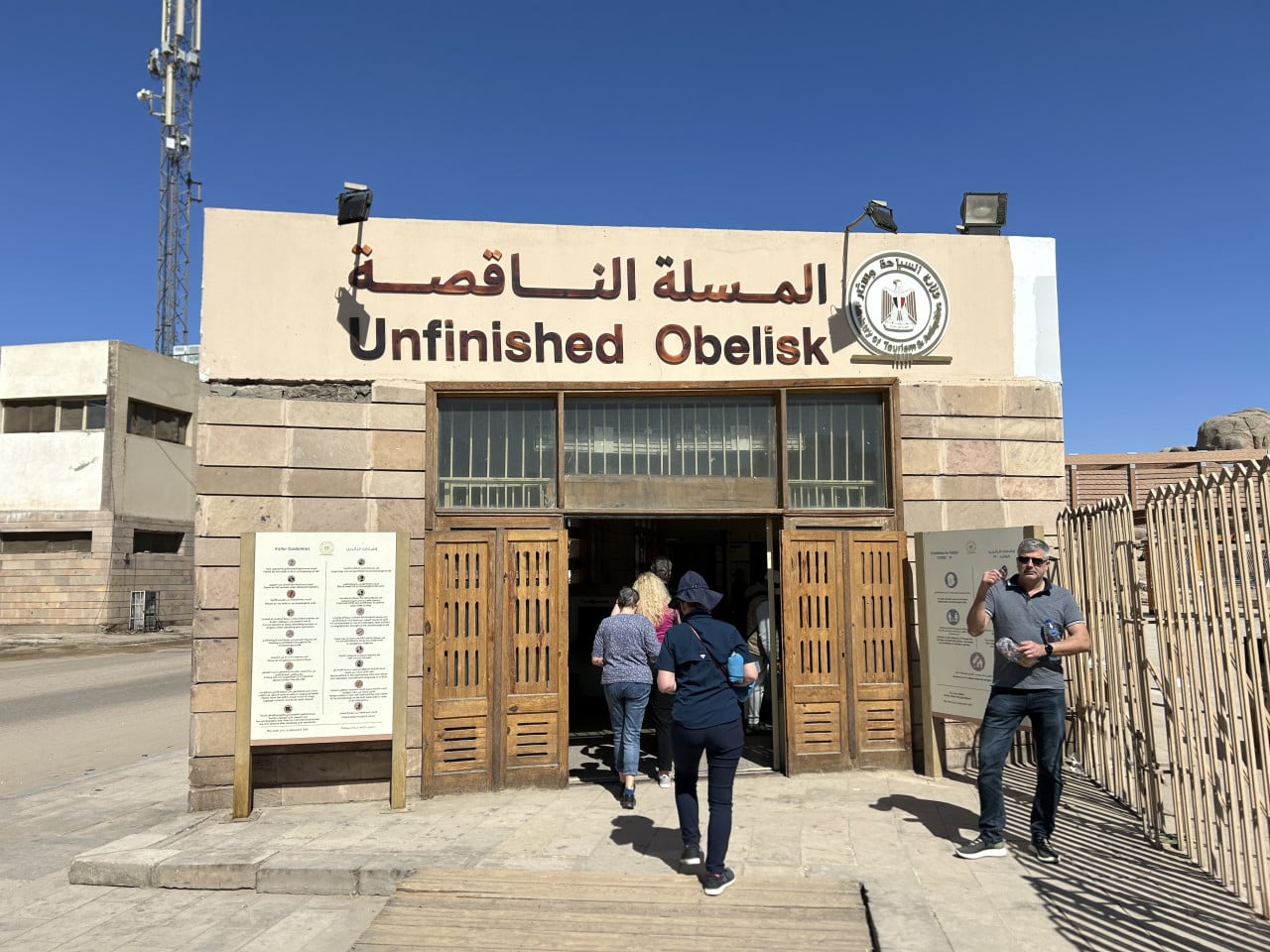 Vstup do památky Unfinished Obelisk v Asuánu s turisty a arabským nápisem.