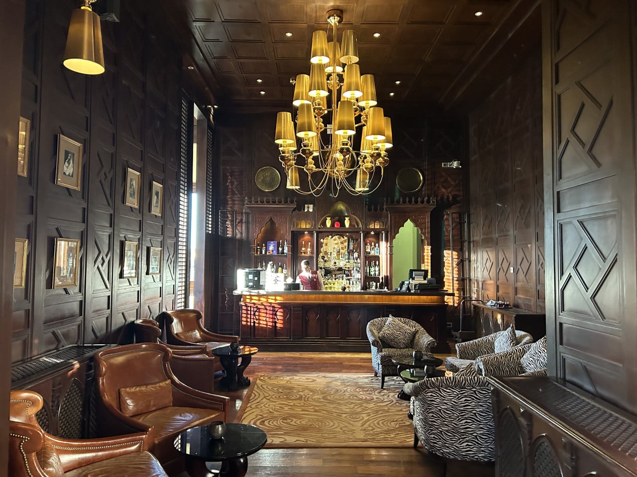 Luxusní hotelový bar s křesly, lustry a dřevěným obložením ve stylu Old Cataract.