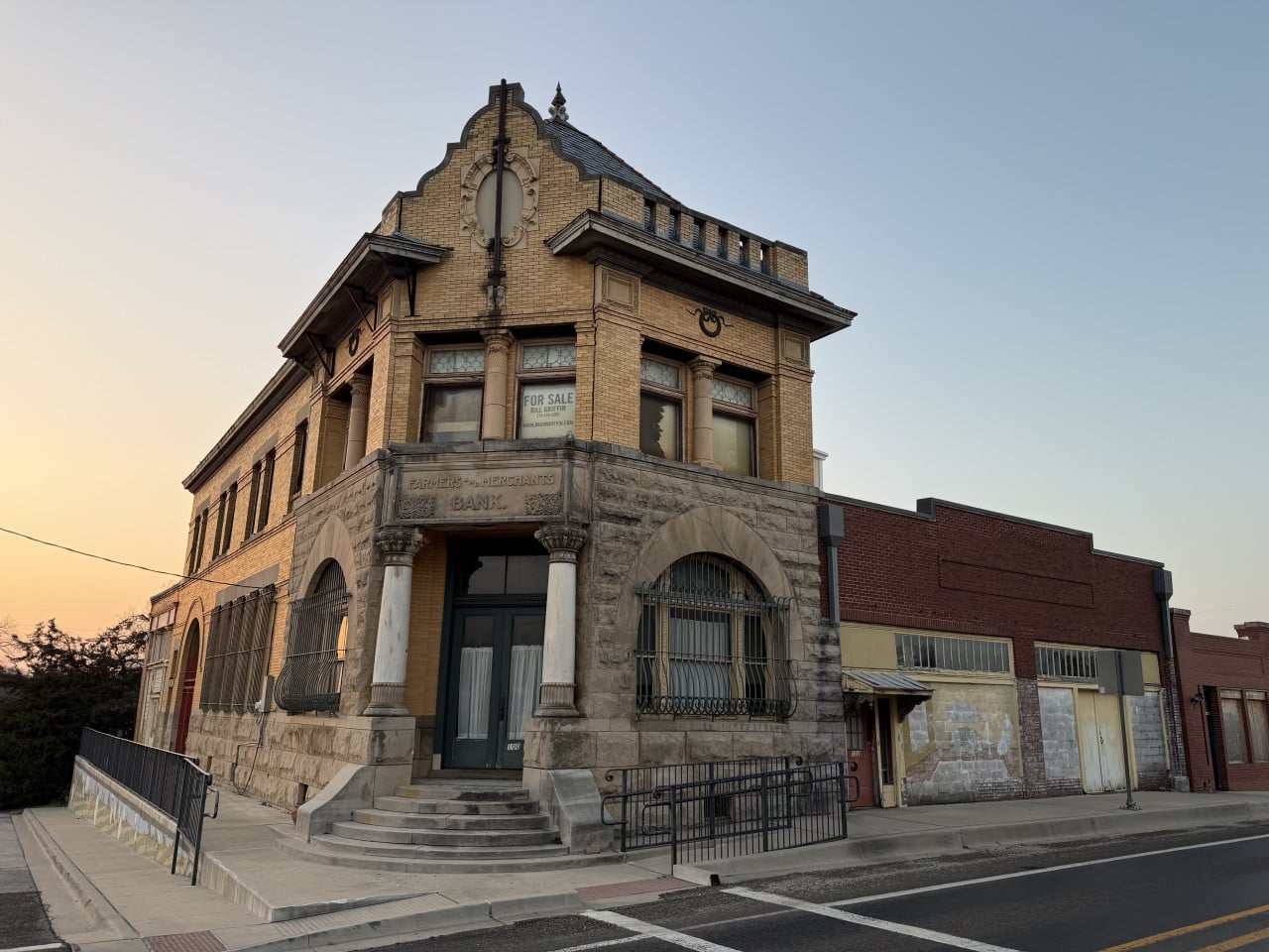 Historická budova Farmers & Merchants Bank, na okně cedule FOR SALE.