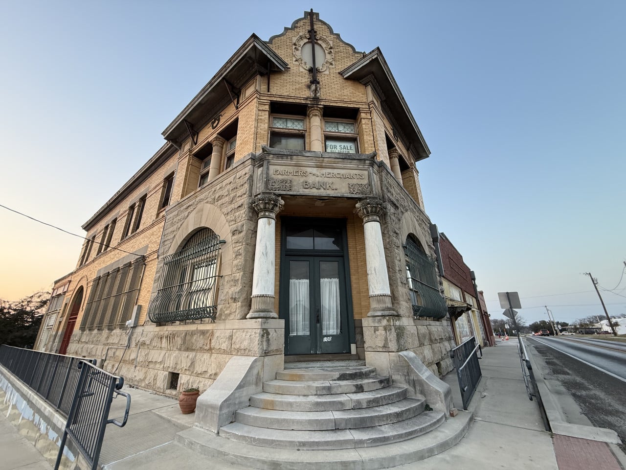 Historická budova Farmers & Merchants Bank, na okně nápis FOR SALE.