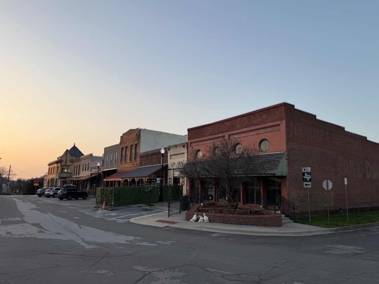 Historické cihlové budovy v centru Pilot Point, zaparkovaná auta, značky STOP a WEST.