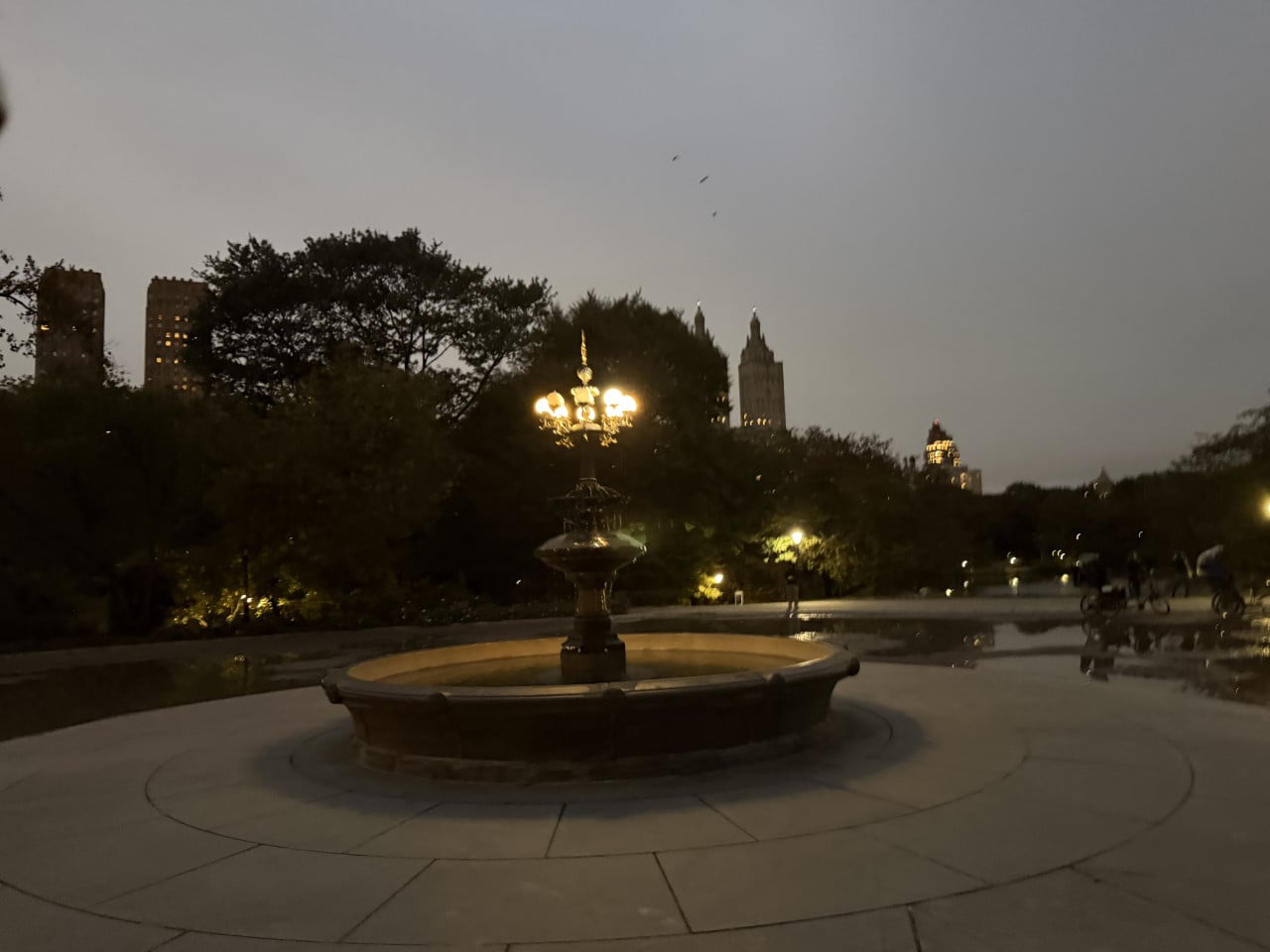 Osvětlená fontána v Central Parku za soumraku s mrakodrapy v pozadí