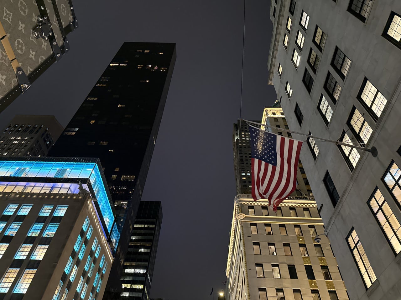 Noční pohled na newyorské mrakodrapy s americkou vlajkou u budovy