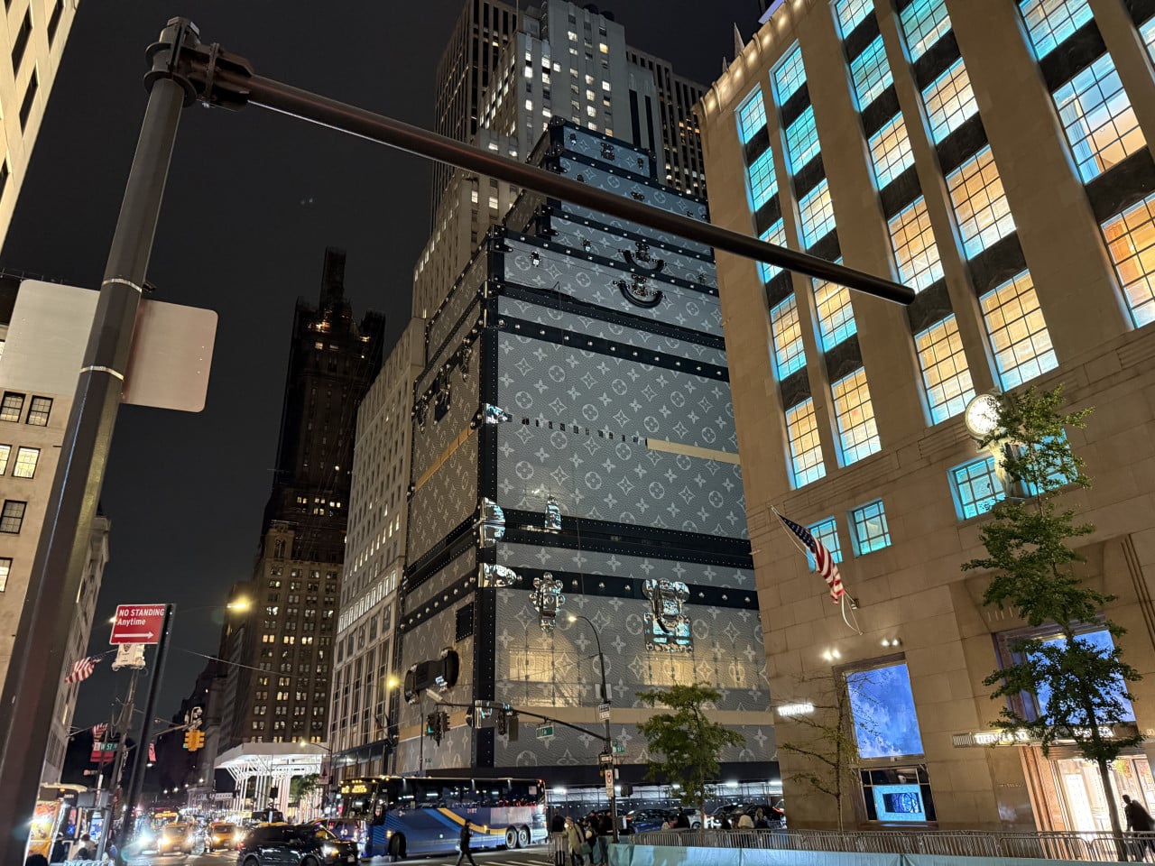 Noční ulice New Yorku s obřím kufrem Louis Vuitton na budově a dopravou.