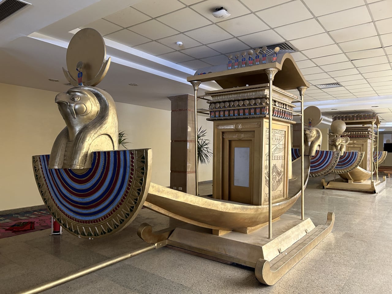 Modely egyptských posvátných bárek s hlavami božstev v muzeální hale