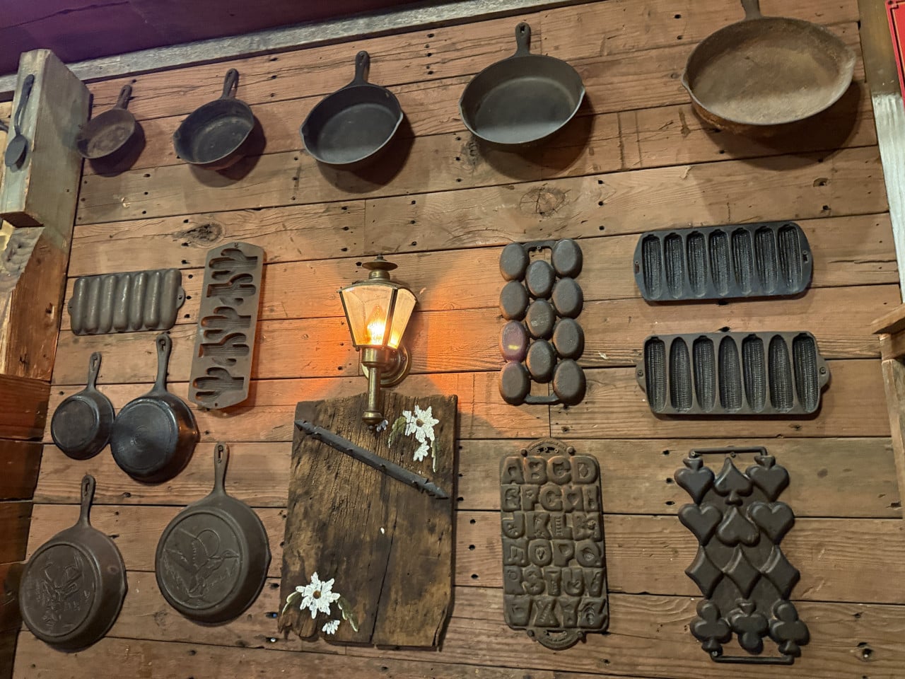 Dřevěná stěna s litinovými pánvemi, formami a svítící lucernou v restauraci
