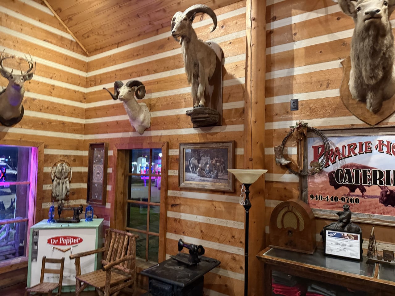 Rustikální interiér s vycpanými trofejemi, cedule Prairie House Catering a lednice Dr Pepper.