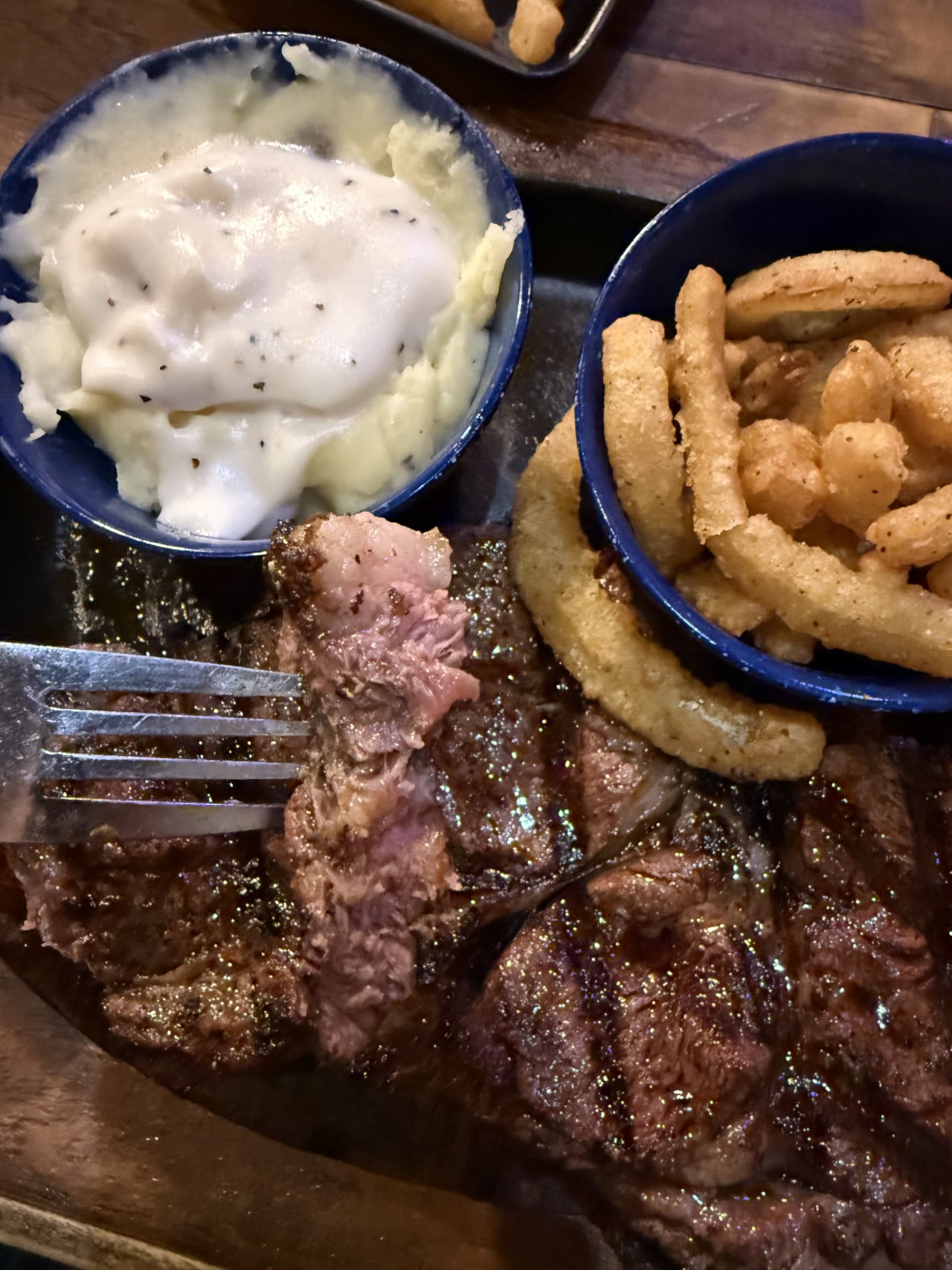 Kousky steaku na talíři, hranolky v misce a kaše s omáčkou.