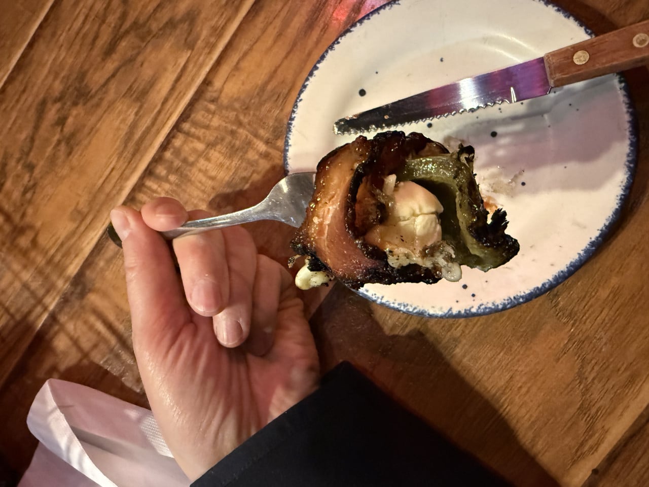 Ruka drží vidličku s kouskem slaniny a grilované papriky nad talířem