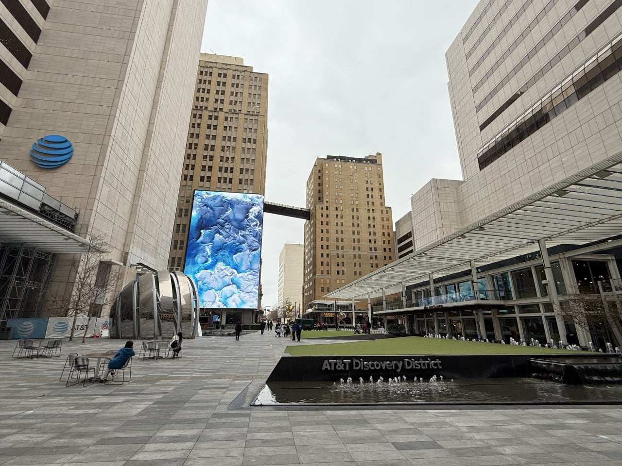 Náměstí v Dallasu s fontánou a nápisem AT&T Discovery District, mrakodrapy a obrazovkou
