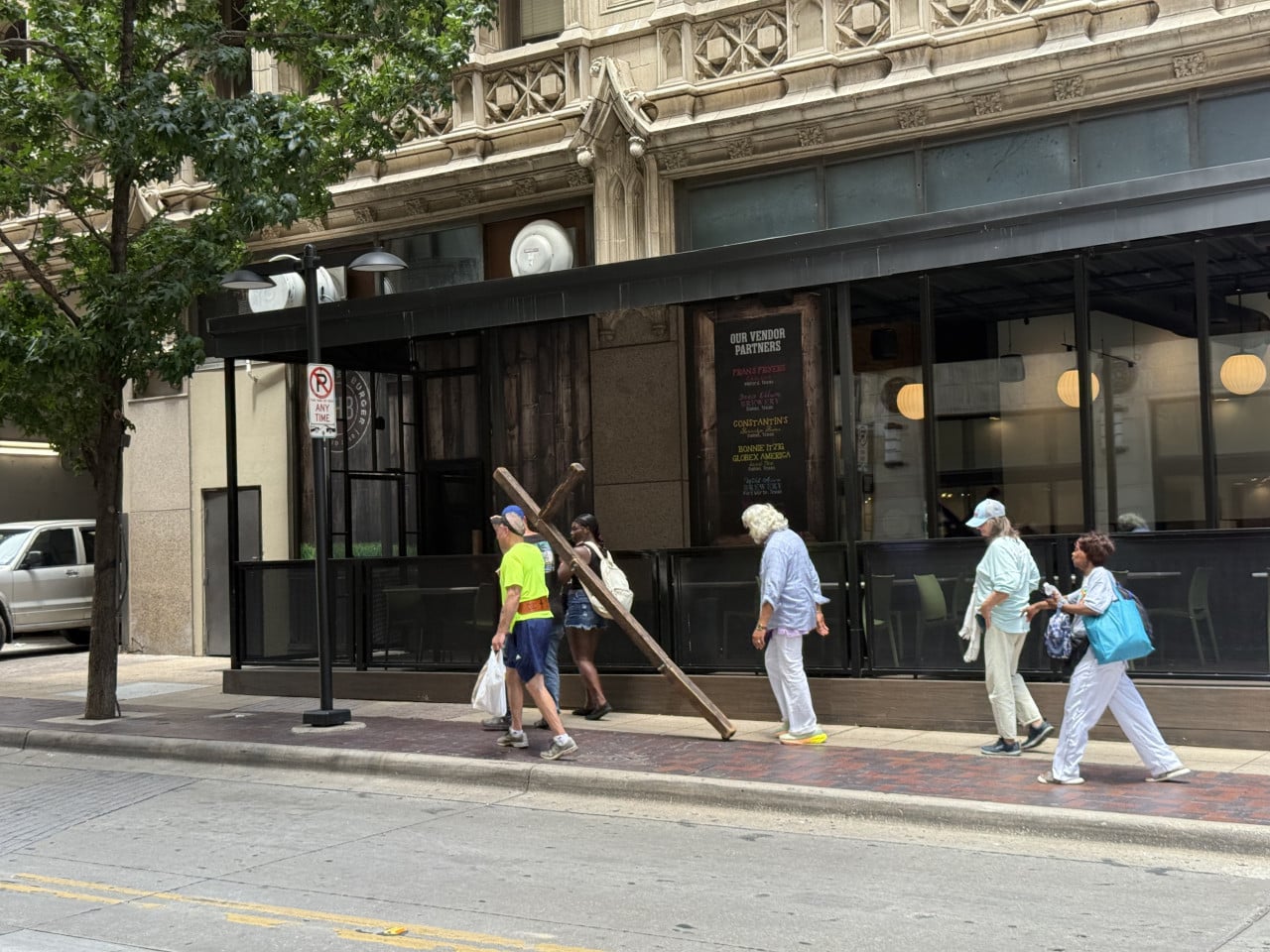 Pěší na chodníku u restaurace, cedule NO PARKING ANY TIME, výloha OUR VENDOR PARTNERS