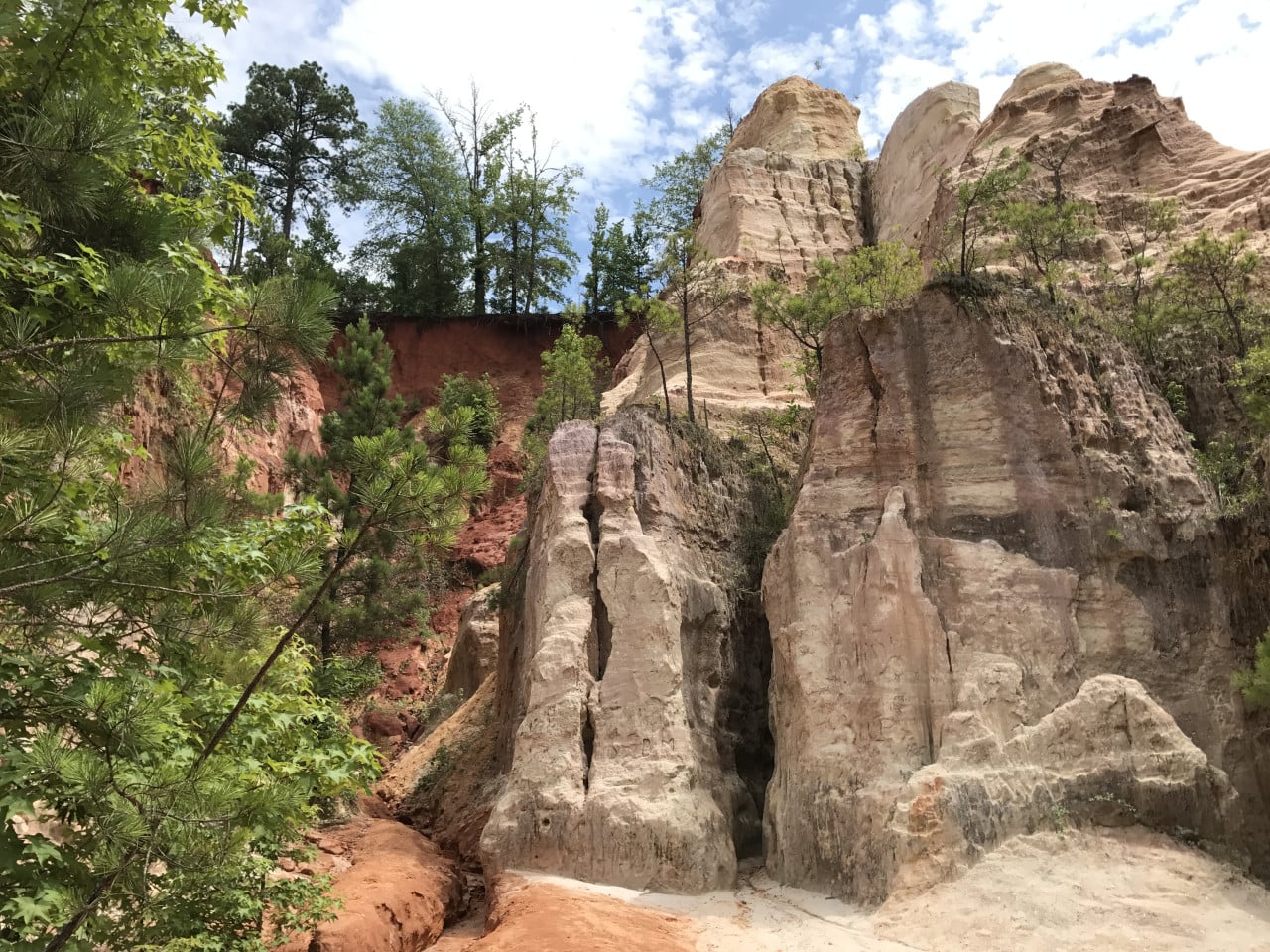 Barevné erodované skalní věže v Providence Canyon obklopené stromy a modrou oblohou