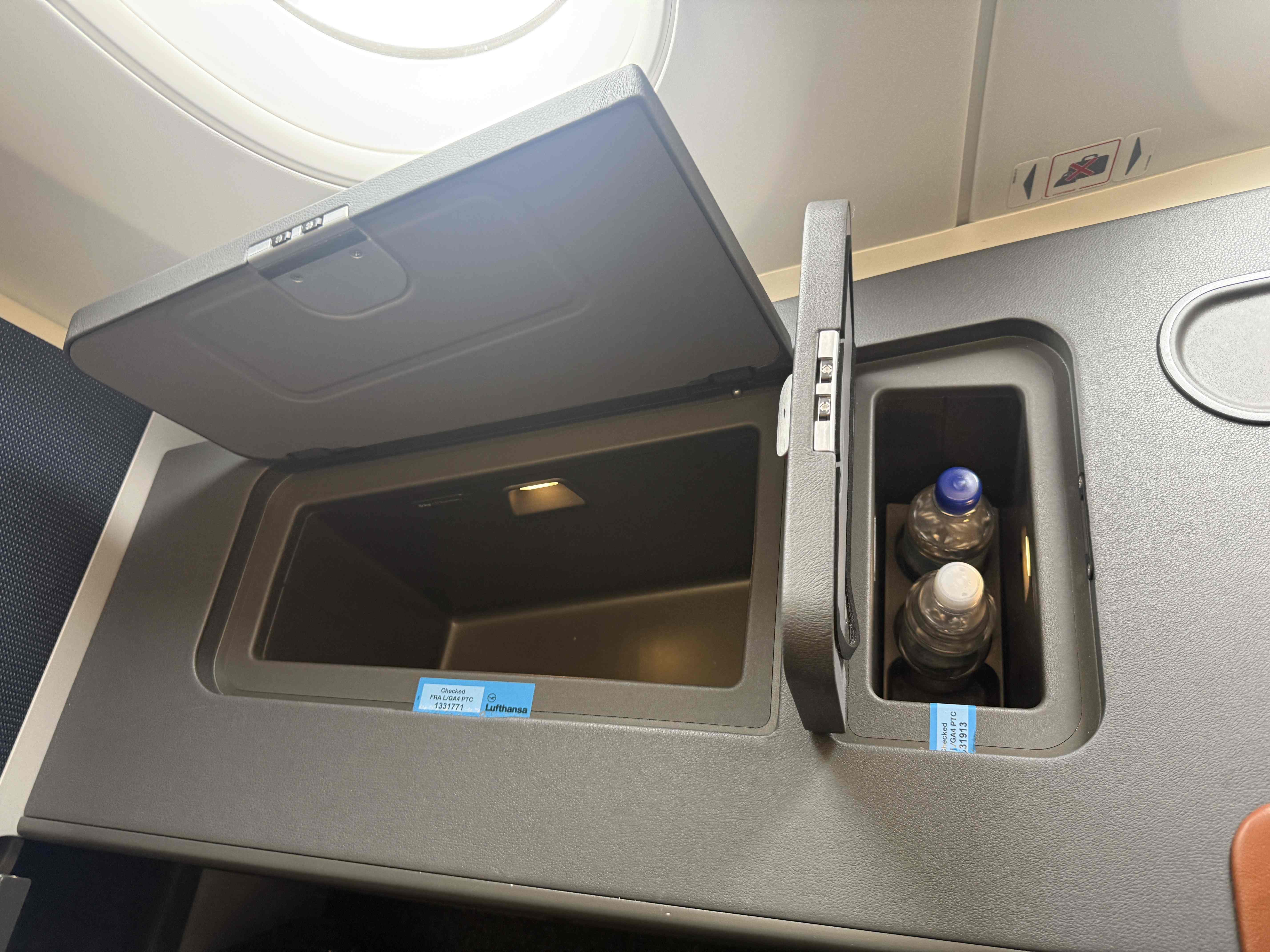 Otevřené úložné schránky u business sedadla, lahve vody, štítek Checked / G4A PTC 131913.