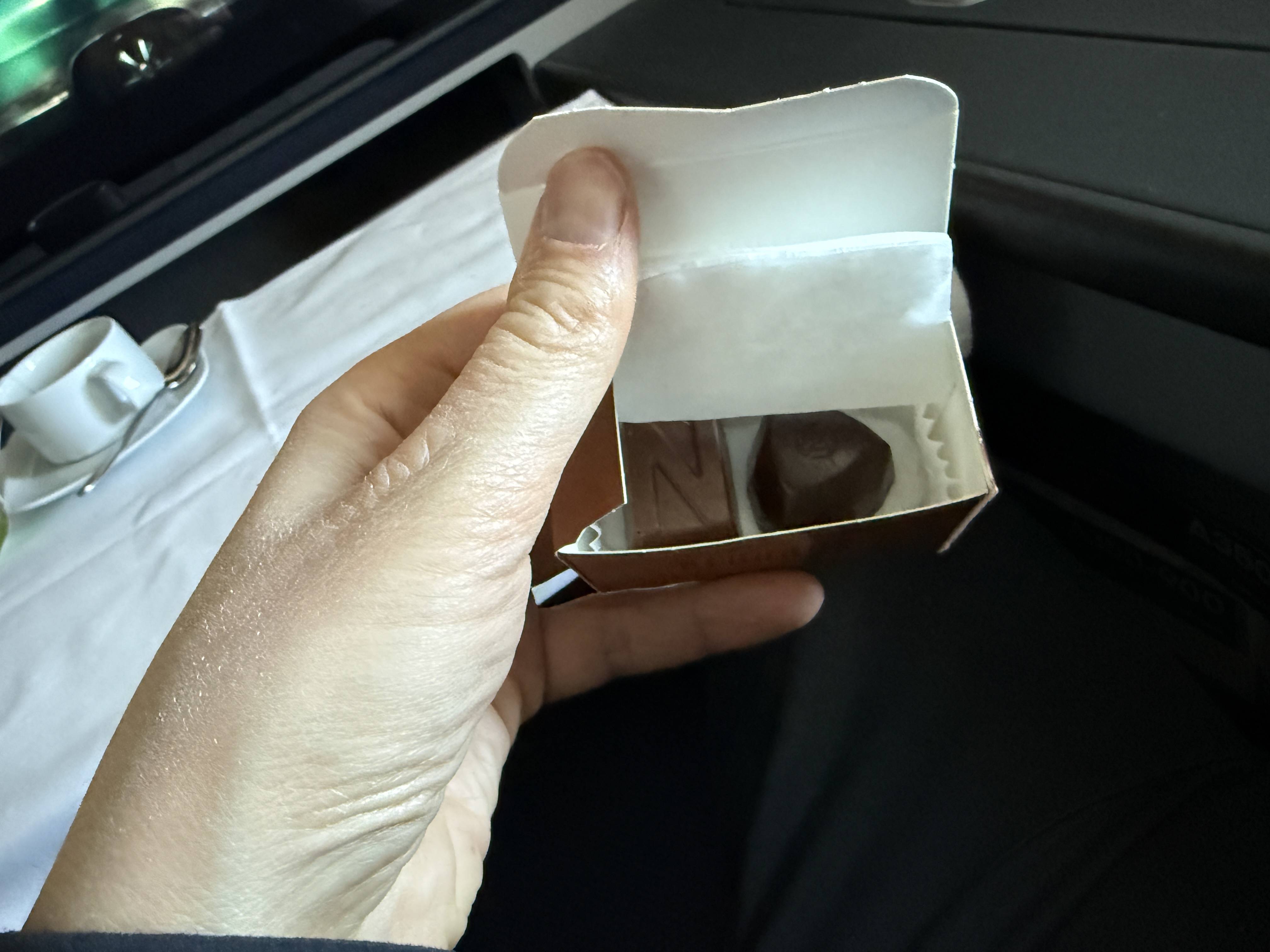 Ruka drží otevřenou krabičku s pralinkami, v pozadí šálek na stolku