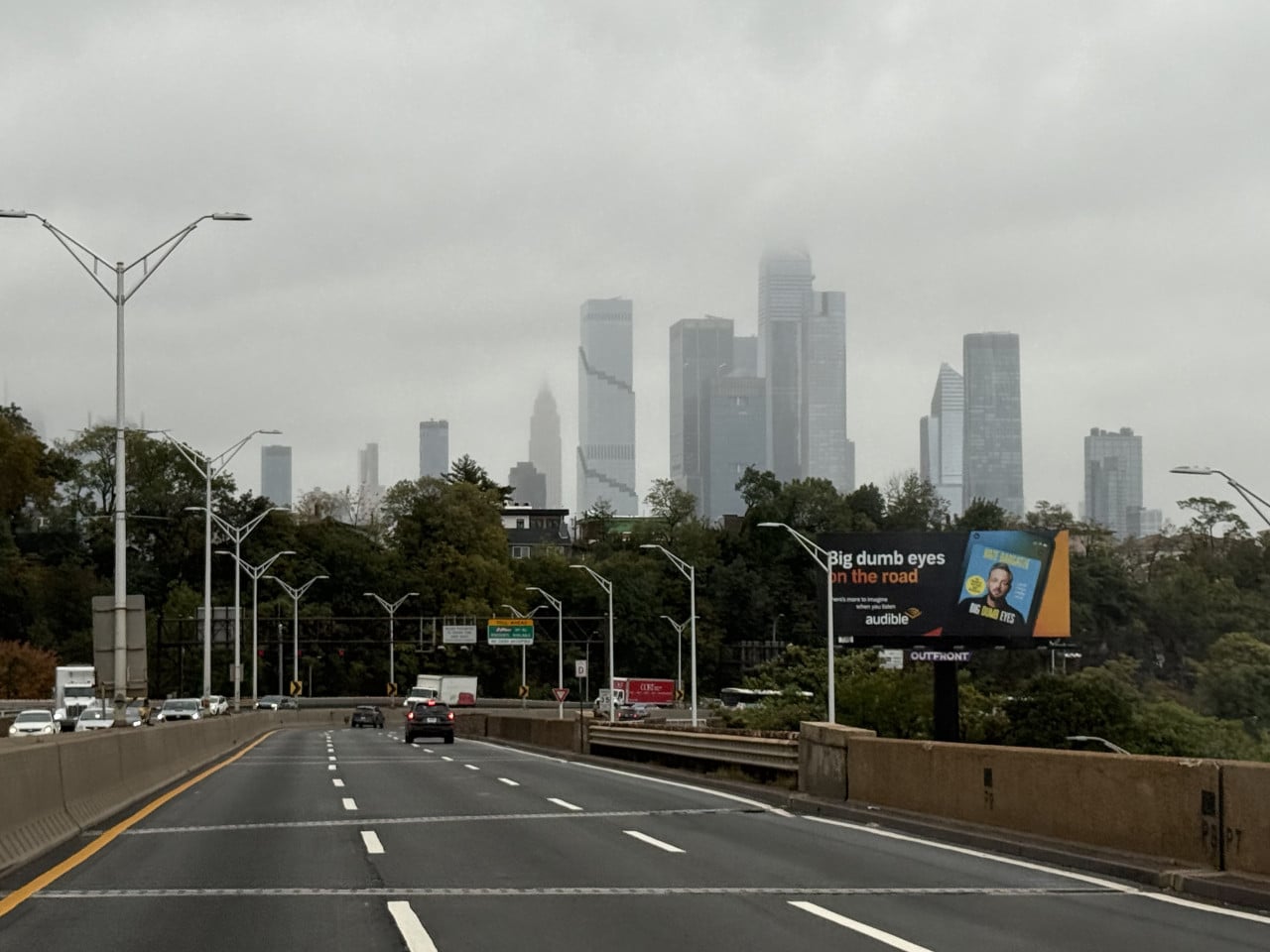 Mlha nad Manhattanem při jízdě po dálnici, billboard Audible v popředí.