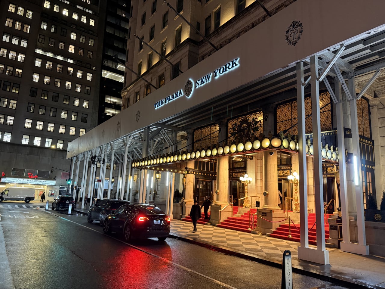 Noční vjezd do hotelu The Plaza New York s červeným kobercem a auty.