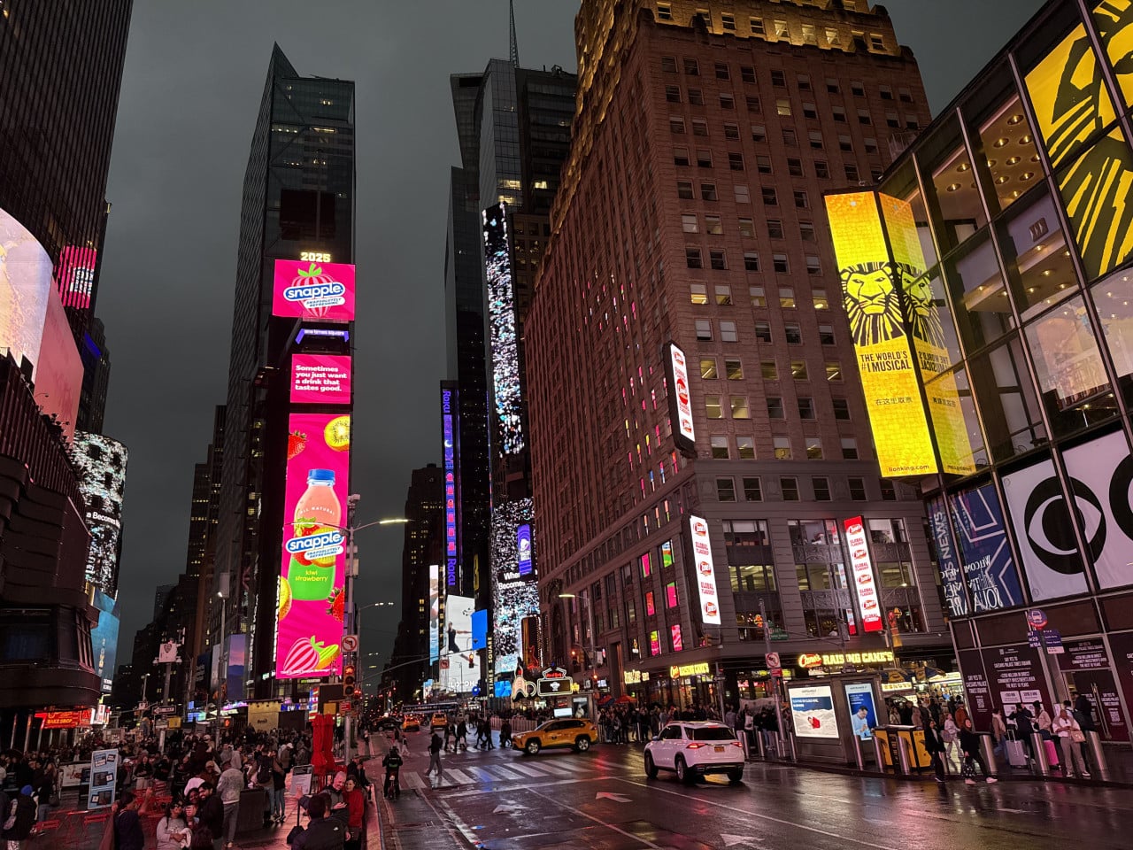 Noční Times Square s neonovými reklamami, ulicí a davy chodců
