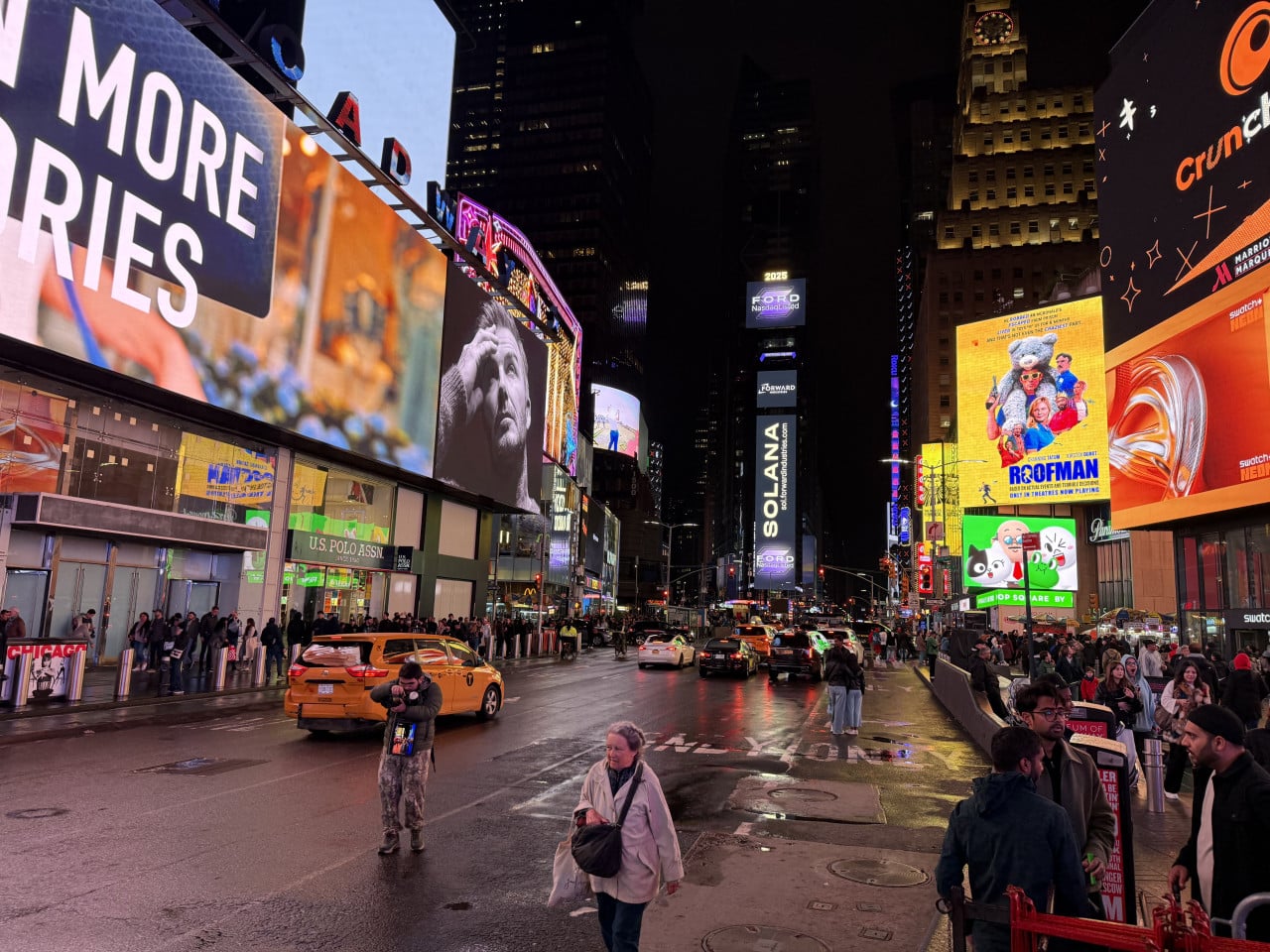Večer na Times Square s neonovými reklamami, taxíky a davy lidí.