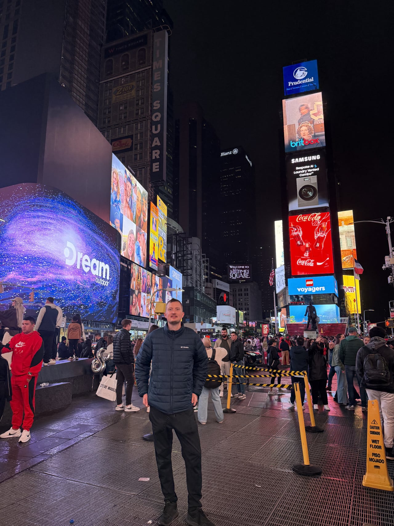 Noční Times Square s davem lidí a jasnými reklamními obrazovkami, muž stojí v popředí.