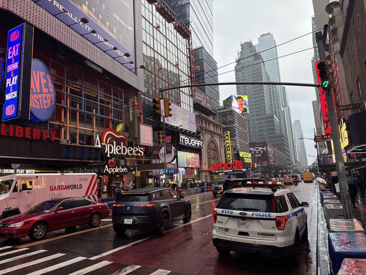 Deštivá Times Square s billboardy, auty a policejním vozem NYPD.