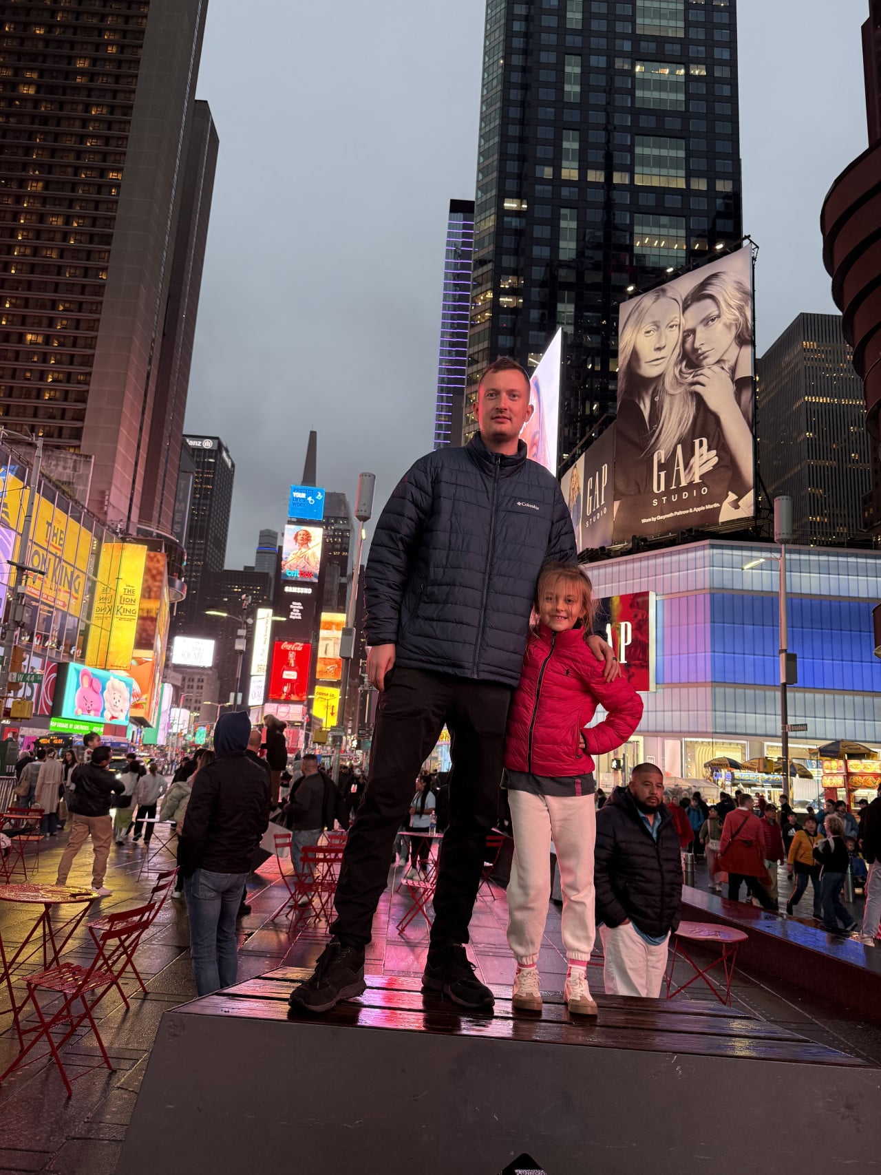 Muž a dívka pózují na Times Square mezi zářícími reklamami a mrakodrapy.