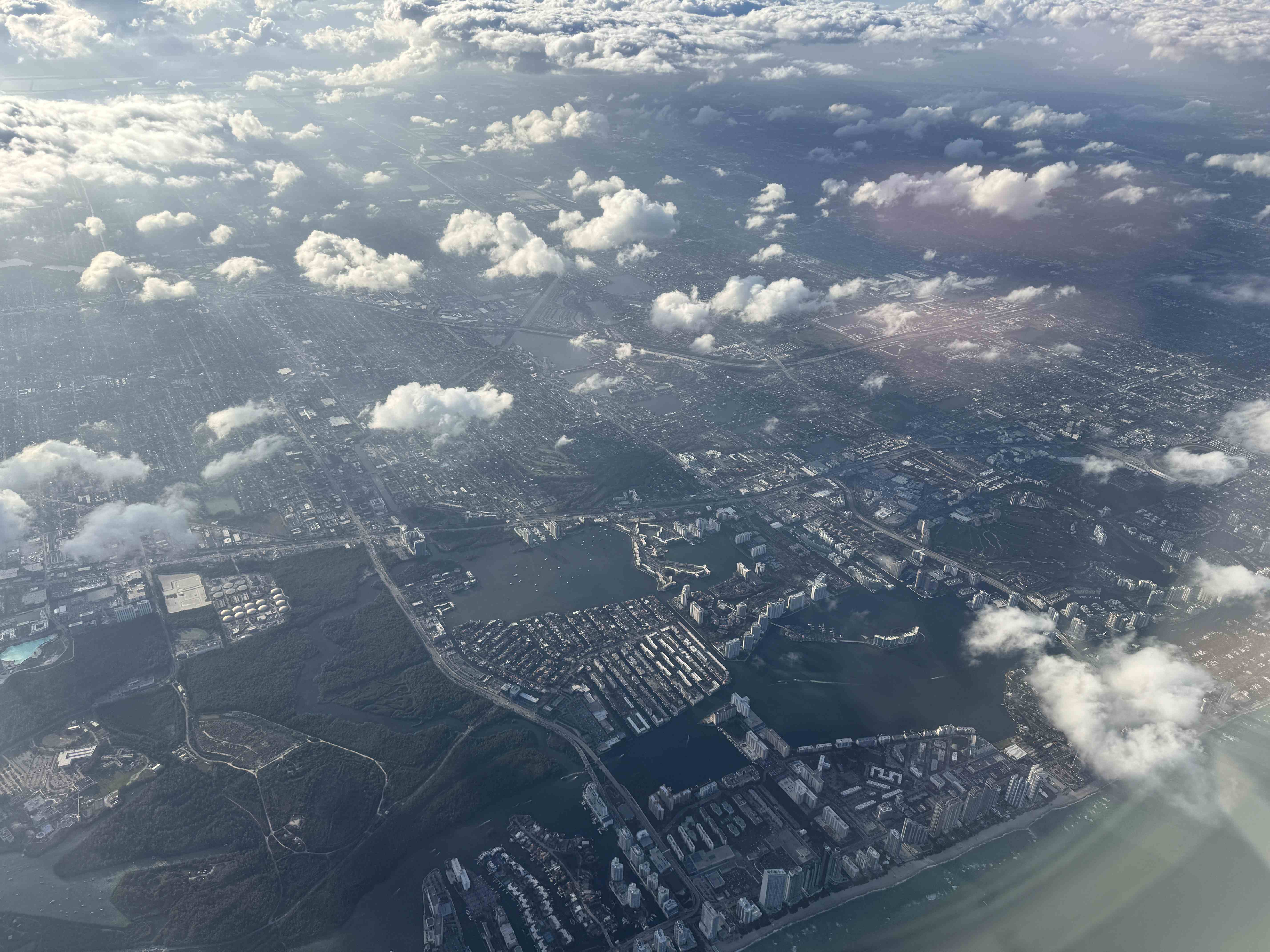 Letecký pohled z okna na město u pobřeží, laguny a rozptýlené mraky