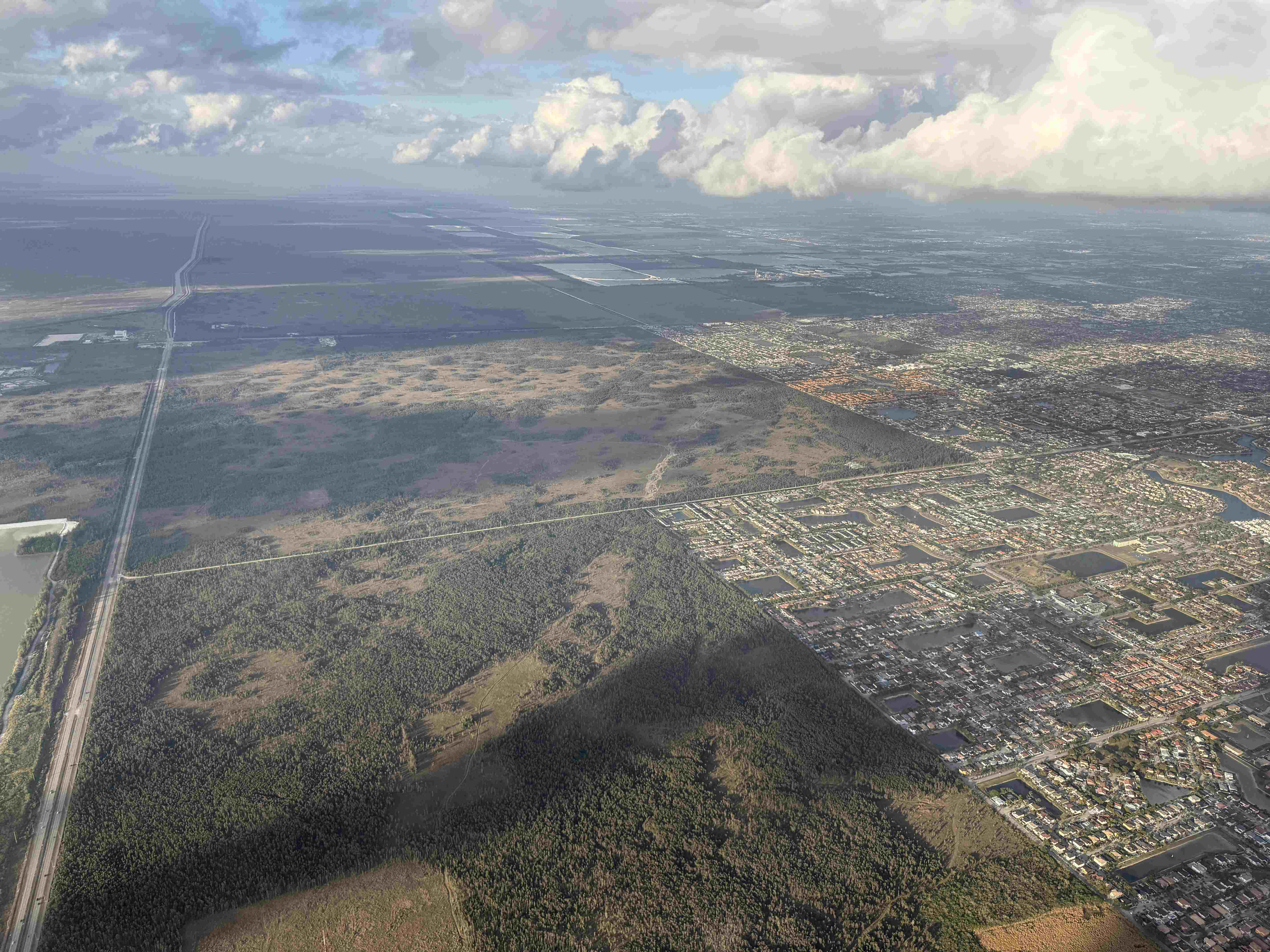 Letecký pohled z okna na les, dálnici a město pod mraky