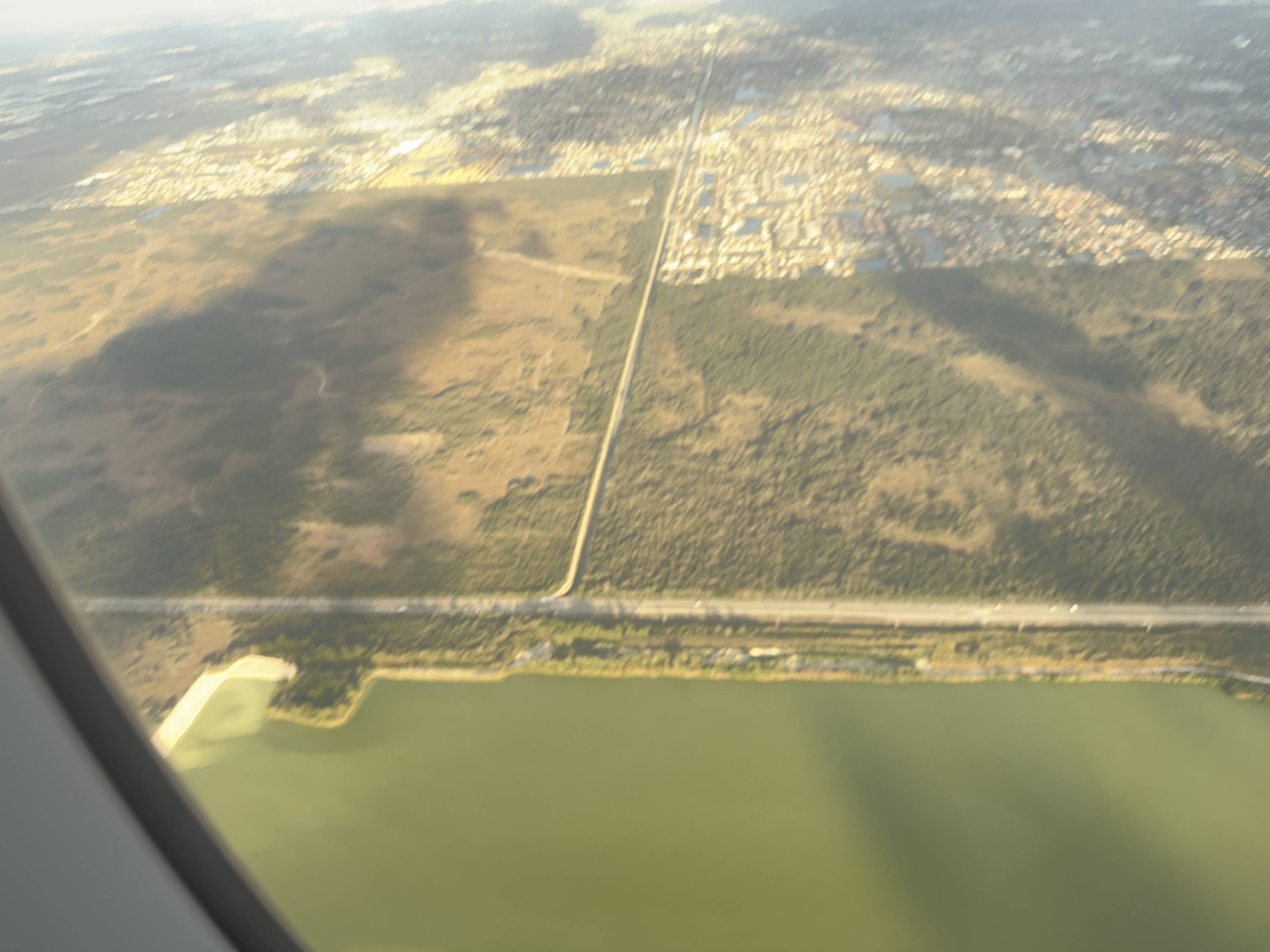 Letecký pohled z okna na jezero, lesy a dlouhou rovnou silnici